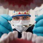 Healthy teeth and smile. Serious doctor directly into the camera. Dentist sitting in the dentist for dental chair and holding a dental drill in hand.