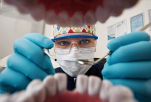 Healthy teeth and smile. Serious doctor directly into the camera. Dentist sitting in the dentist for dental chair and holding a dental drill in hand.